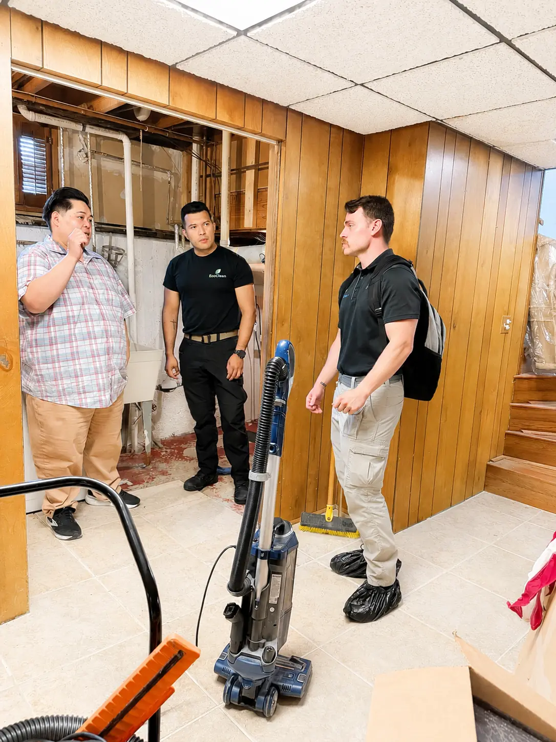 Two EcoClean technicians talking with a man in a partially demoed basement.