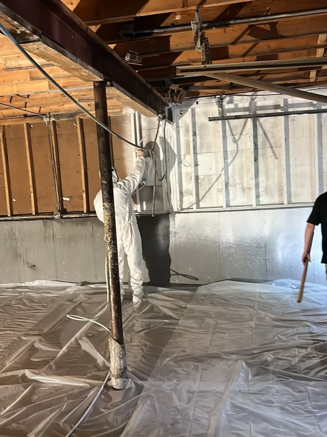 Technician in a protective suit in a gutted basement with the floor covered in plastic sheeting.