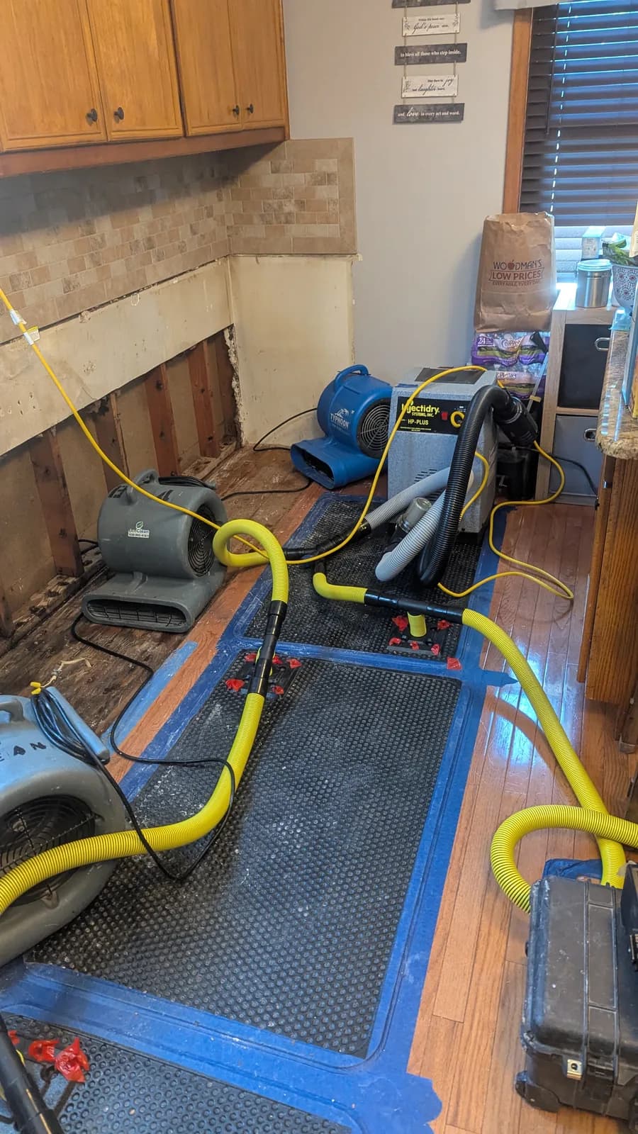 Floor-drying mats and hoses taped down on kitchen hardwood.