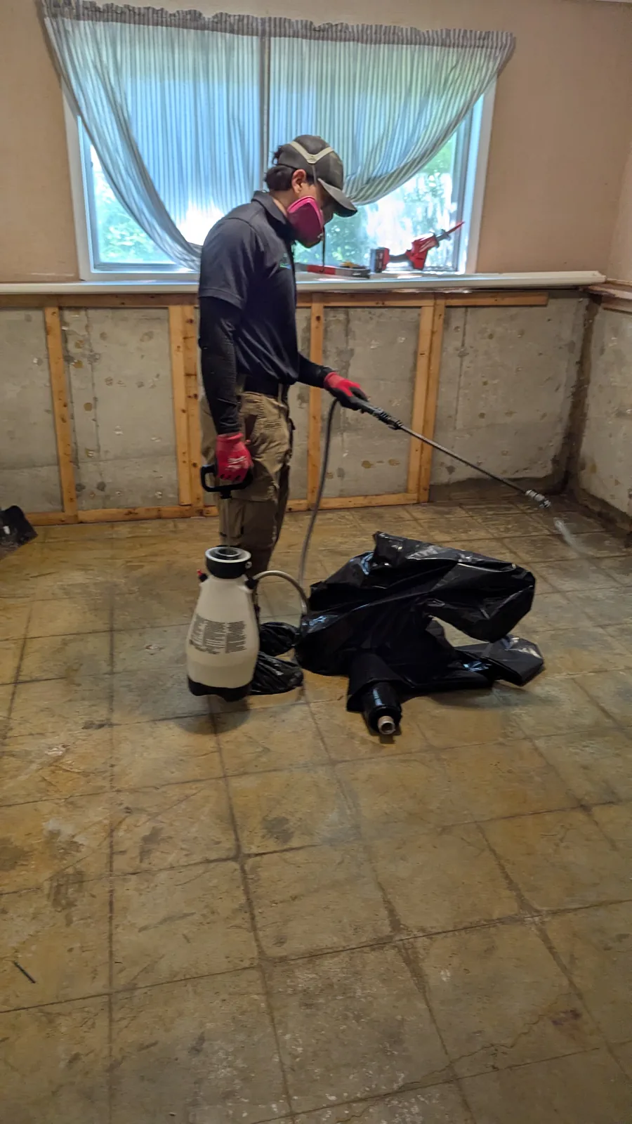 Technician wearing a respirator treating a wall in a gutted kitchen.