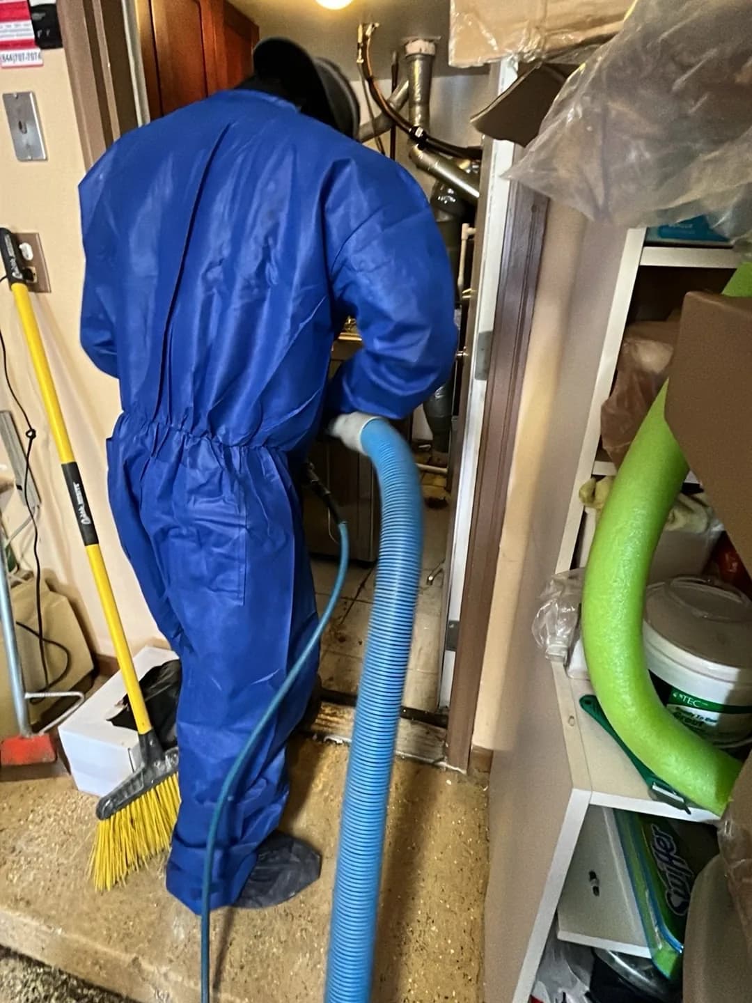 Technician in a full protective coverall running an extraction hose in a utility area.